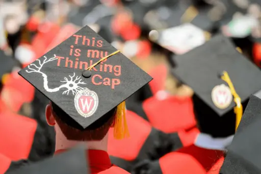 back of student wearing graduation cap with "This is my thinking cap" on the top