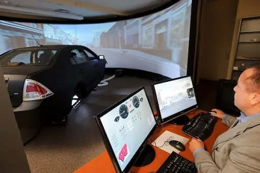 Researcher running driving simulation software next to car with wrap around screen
