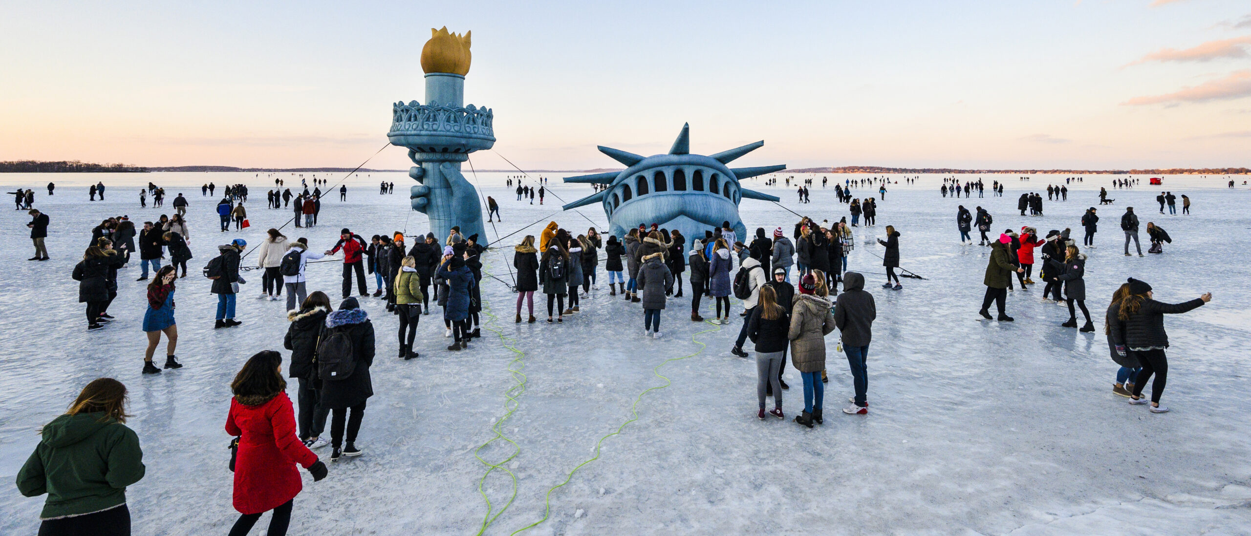 Students standing on frozen lake with Statue of Liberty head stick above the ice