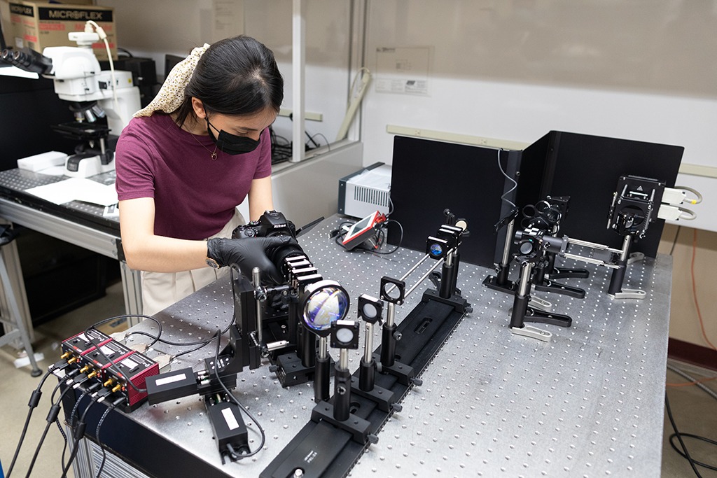PhD student sets up an optics experiment on an optics table in lab