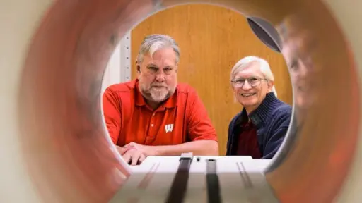 Frank Rath and Bruce Thomadsen, professor of medical physics, looking through the opening of a piece of radiotherapy treatment equipment