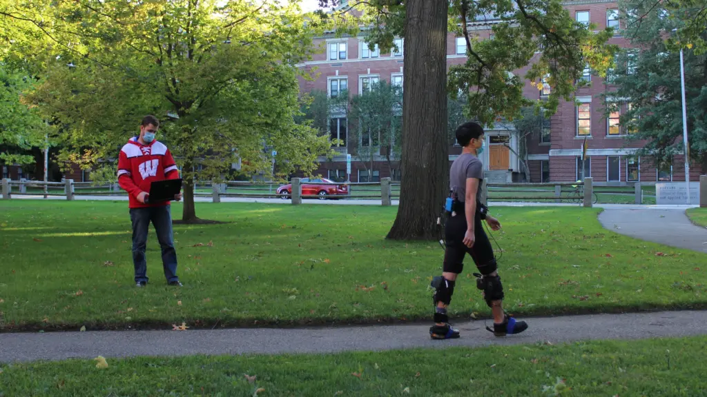 A person walks outside wearing an exosuit and tensiometer