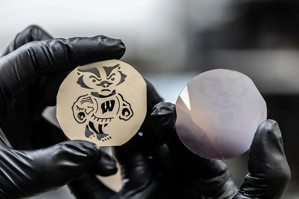 Two black gloved hands each holding a metal disc with image of Bucky Badger from UW-ECE Kats lab