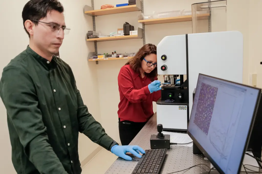 Assistant Professor Filiz Yesilkoy places a sample in a microscope while PhD student Samir Rosas works at the computer.
