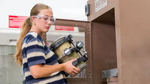 Civil and environmental engineering junior Ella Thomas loads a 100-year-old concrete sample into a hydraulic press for testing.