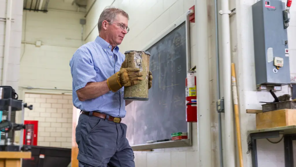Steven Cramer, a civil and environmental engineering professor emeritus, carries a fractured concrete sample after testing it in a hydraulic press.