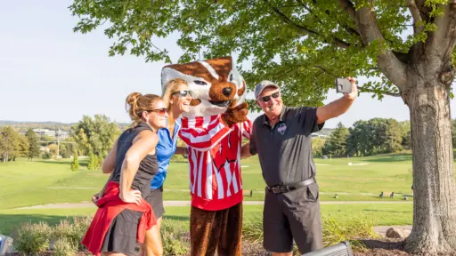 Golfers pose on the golf course for a selfie with Bucky Badger.
