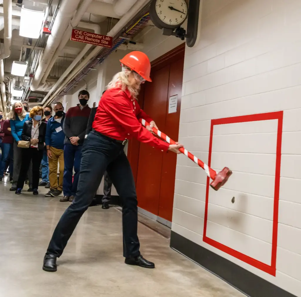 Regina Murphy wields a sledge hammer  against a wall to celebrate the brick breaking ceremony