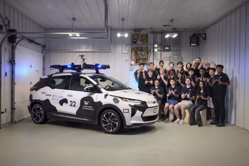 Wisconsin Autonomous team poses with cow-spotted autonomous vehicle