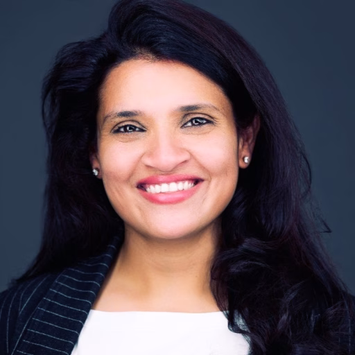 Woman with dark hair wearing a white collarless shirt under a blazer