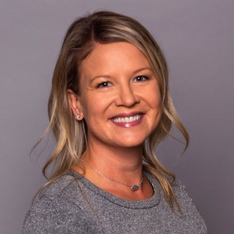 early career woman with light hair wearing a necklace and light grey sweater