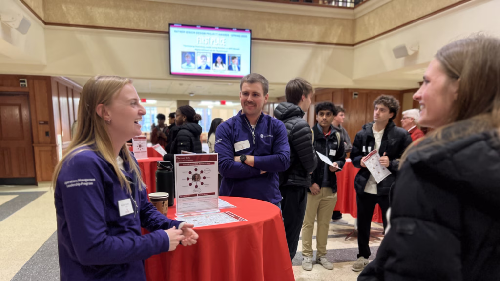 Group of young adults standing and laughing around a cocktail table with a red tablecloth