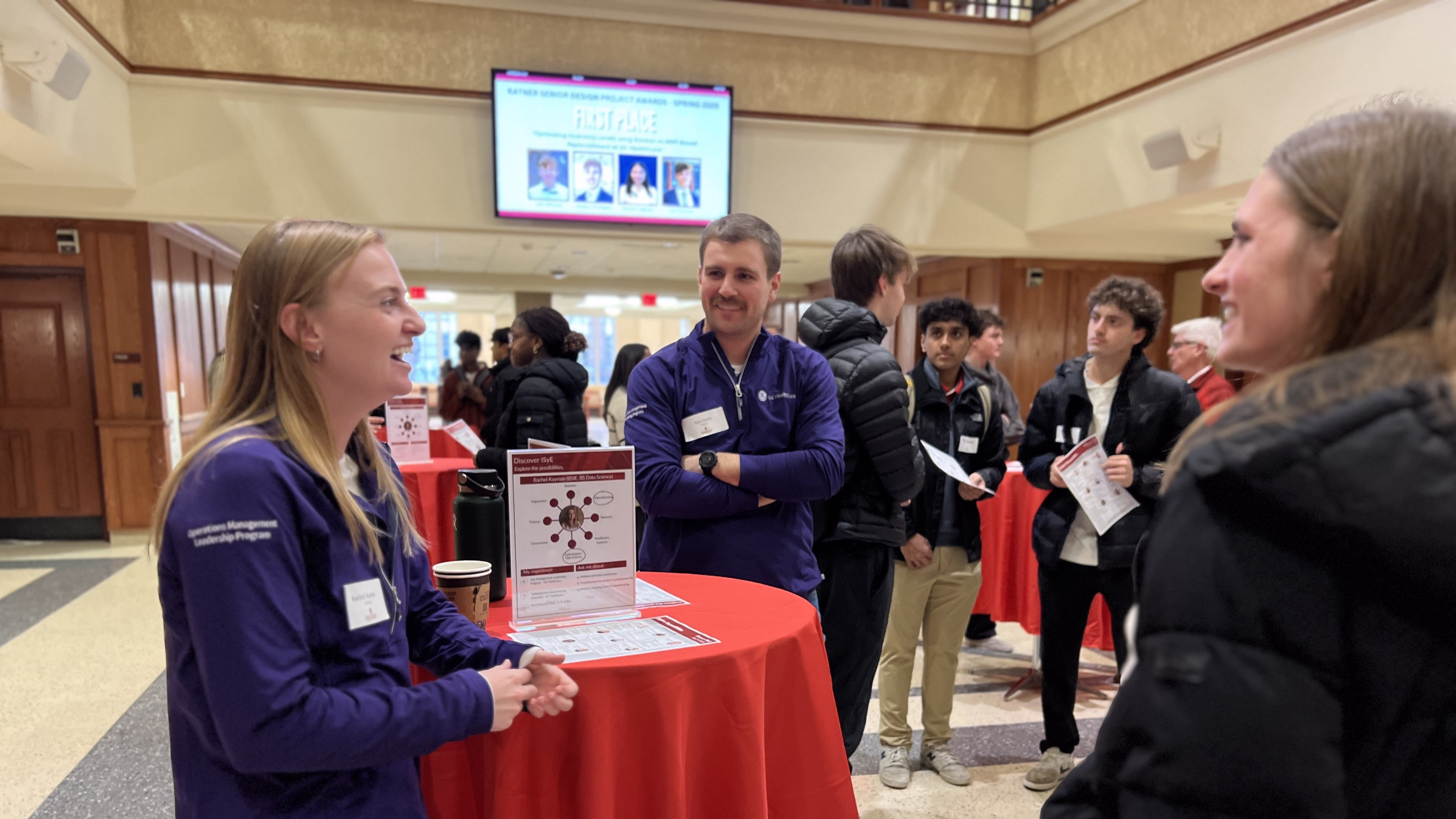 Group of young adults standing and laughing around a cocktail table with a red tablecloth