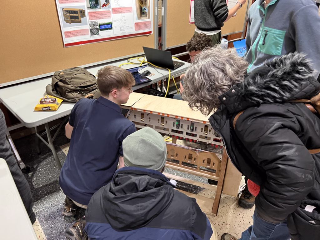Student kneeling in front of vending machine project while one man and one woman look closely at the project