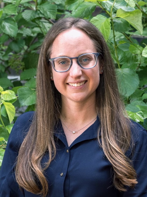 Profile photo of Alexandra Bayles. She has long brown hair and is wearing glasses and a blue button down.