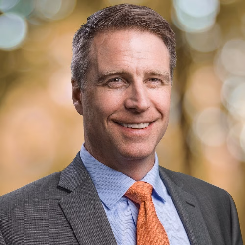White mid-career man wearing a grey suit and orange tie