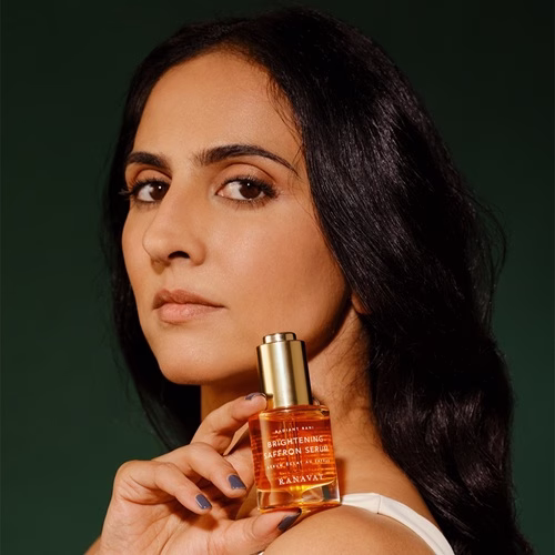 Indian-American woman looking sideways over her left shoulder holding a beauty product