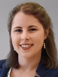 Early career white woman with shoulder-length brown hair wearing pearl earrings and a blue blazer