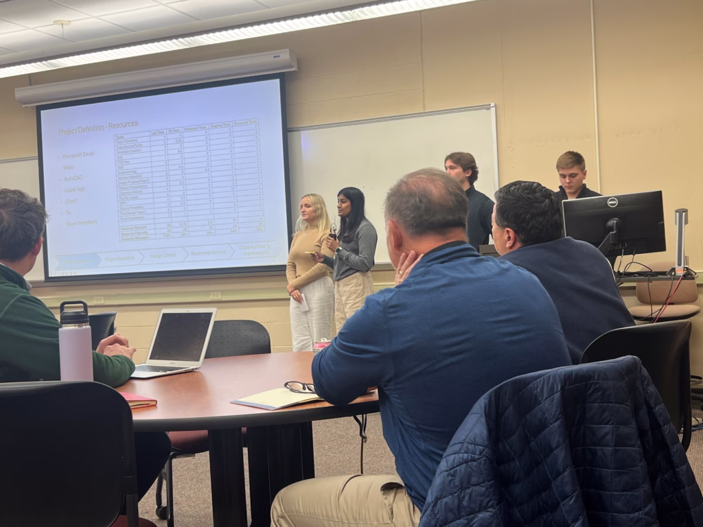 Industry professionals sitting at a table observing a presentation by college students