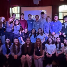 A large group of college students posing together on a low indoor stage