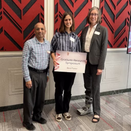 Student holding award sign stands between two professors