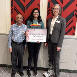 Student holding award sign stands between two professors