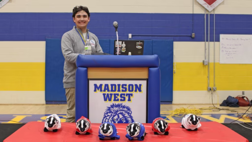 William Noguera standing behind a podium in the gym of Madison West High School during the Badger Invitational.