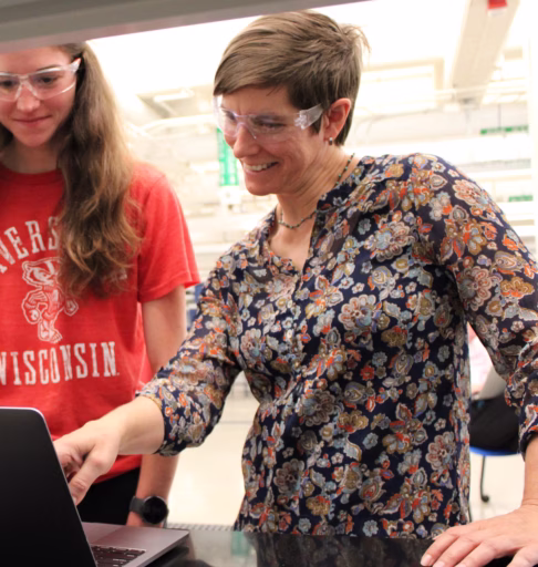 Profile photo of Natasha Mallette in front of lab bench with student. She has short hair and is wearing a patterned blouse.