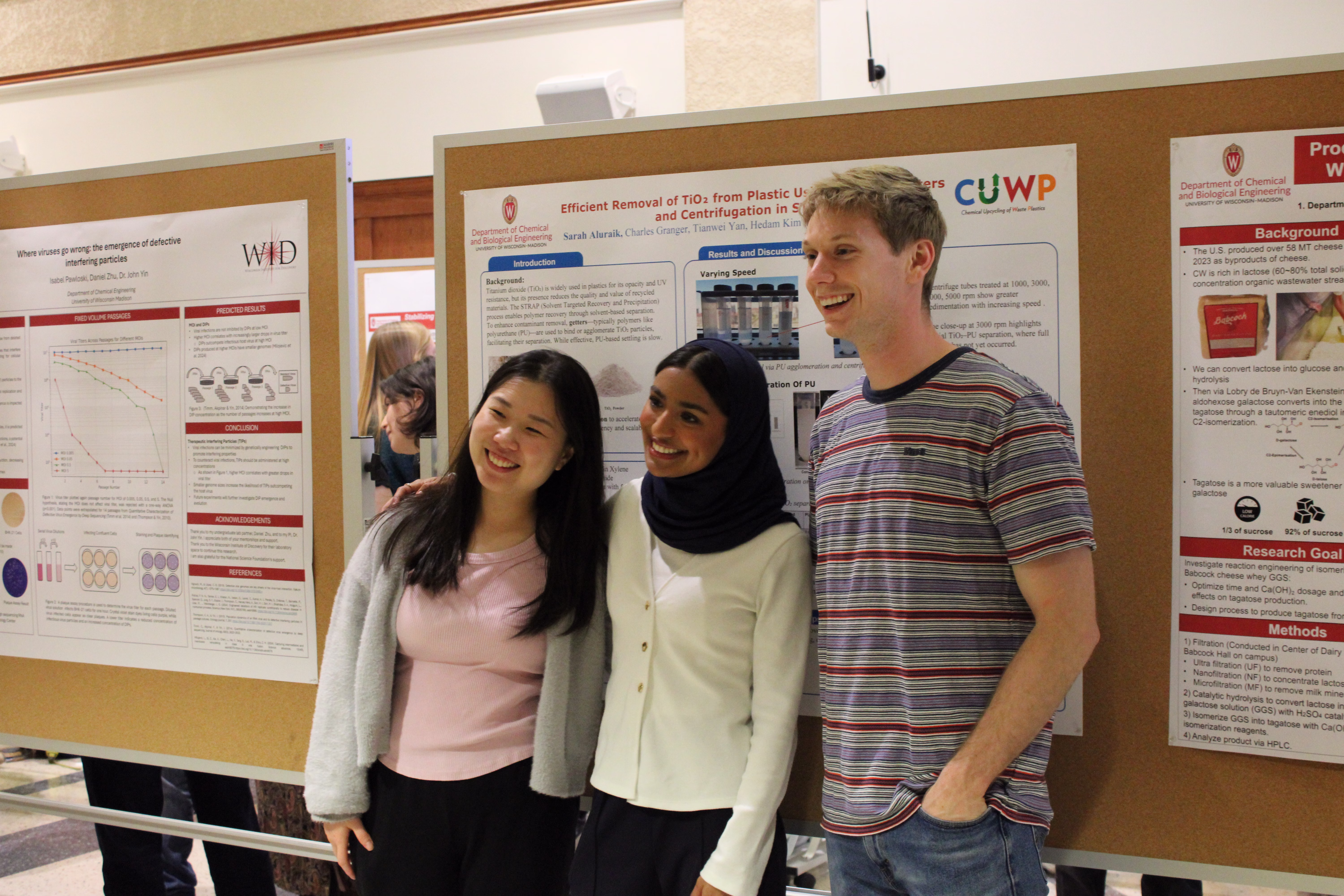 Three students stand in front of research poster, which is pinned to a cork board.